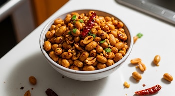 Un tazón de maní picante al ajo con trozos de chile seco y cilantro fresco picado, reposa sobre una superficie blanca de cocina con buena iluminación.