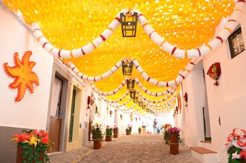Calle empedrada decorada con un techo amarillo de papel, guirnaldas blancas con faroles y macetas con flores de papel en los laterales