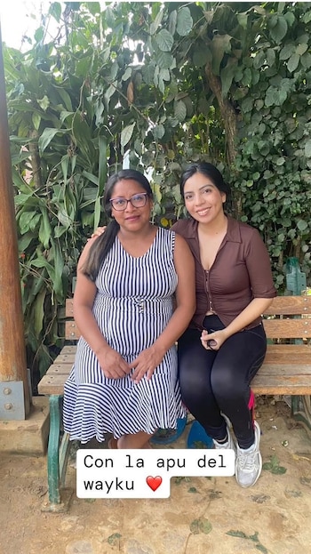 Dos mujeres sentadas en un banco de madera. Fondo de vegetación. Una mujer viste un vestido de rayas, la otra una blusa marrón. En la parte inferior, un texto y un corazón