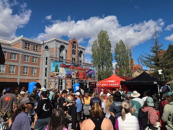 Multitud de personas se congrega en un evento al aire libre. Un cartel de "Cocodona 250" domina el fondo con edificios de ladrillo y tiendas