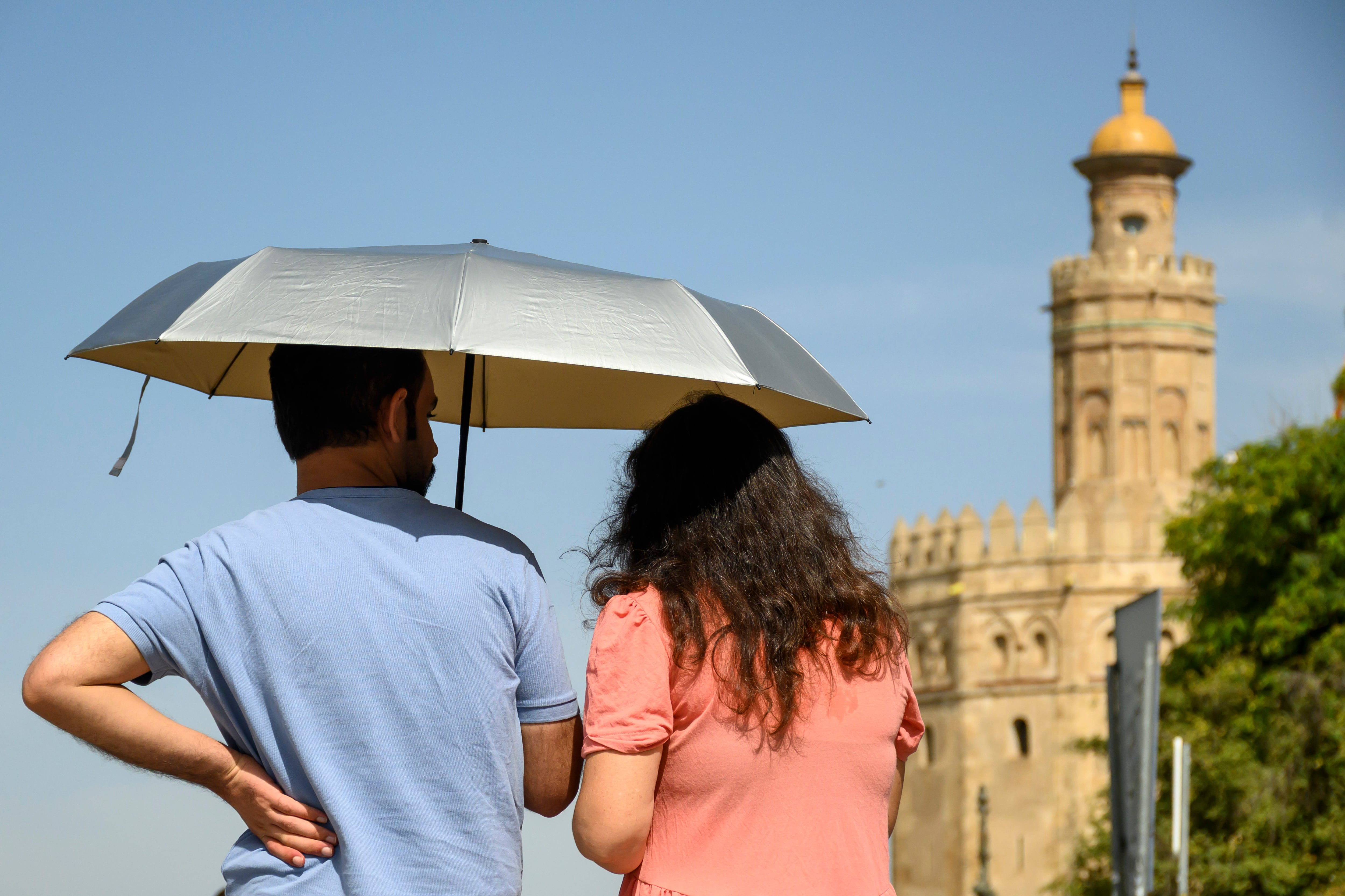 Una pareja pasea por Sevilla bajo una sombrilla, este jueves. (EFE/Raúl Caro)
