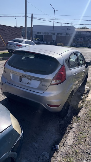 Un automóvil gris estacionado junto al cordón de una calle asfaltada frente a unos edificios