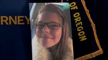 Retrato impreso de una mujer sonriente con gafas frente a un fondo azul oscuro con letras doradas y una bandera con flecos