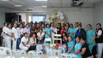 Un grupo de trabajadores de la salud rodea a una persona que sostiene a un bebé en un recinto decorado con globos y regalos