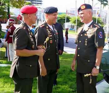 Tres hombres con uniformes militares de color verde oscuro, beretas (una roja y dos negras), insignias y medallas. Uno sostiene un bastón