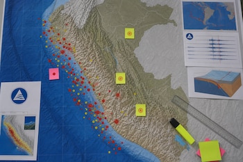 Mapa de Perú con puntos rojos y amarillos en la costa, notas adhesivas, una regla, un marcador fluorescente y hojas con sismogramas.