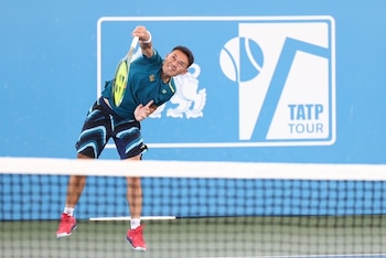 Un jugador de tenis salta sobre la red con una raqueta de tenis en una cancha azul. Al fondo, un muro azul con el logo TATP Tour