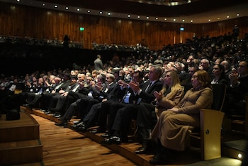 Un auditorio lleno de personas sentadas, muchas aplaudiendo. En las filas delanteras, se ve a Javier Milei entre otros asistentes, algunos con atuendos judíos