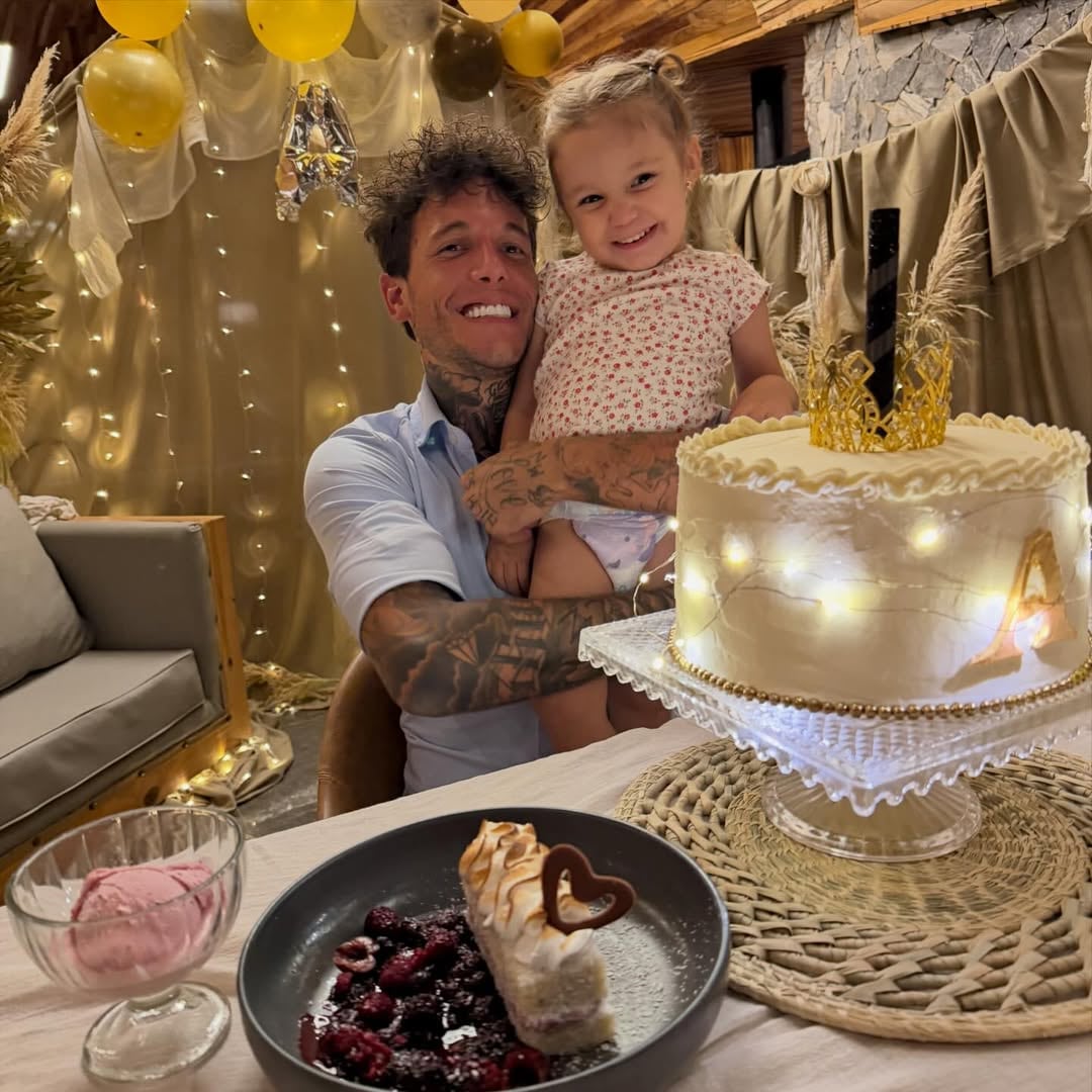 Alex Caniggía sonríe feliz mientras sostiene a su hija Venezia en su cumpleaños número 33, con un pastel decorado y postres en una mesa festiva.