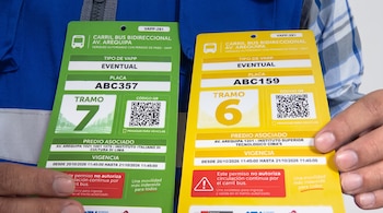 Una persona con chaleco sostiene dos tarjetas de autorización vehicular en colores verde y amarillo con datos impresos y códigos de respuesta rápida.