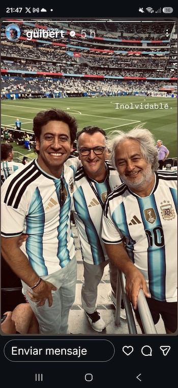 Tres hombres sonríen y visten camisetas celestes y blancas de fútbol con el escudo de Argentina en un estadio lleno de espectadores