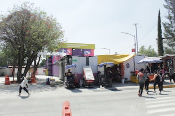 Calle con vendedores ambulantes, peatones, un letrero de "Biciestacionamiento Universidad" y conos naranjas. Un árbol frondoso a la izquierda y edificios al fondo