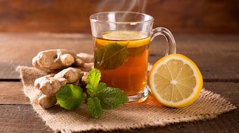 Taza de infusión caliente con limón y menta. Raíces de jengibre, medio limón y ramitas de menta sobre un trozo de tela de yute.