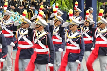 Soldados con uniformes de gala azules y rojos, guantes blancos y plumas de colores en los sombreros marchan y realizan el saludo militar