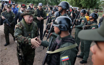 Un oficial militar vestido de camuflaje con sombrero saluda a un soldado venezolano uniformado con casco. Otros soldados armados se alinean detrás