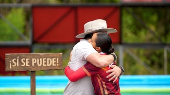 Un hombre con sombrero abraza a una mujer con uniforme rojo junto a un letrero de madera con la leyenda "¡SÍ SE PUEDE!".