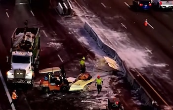 Vista aérea de un accidente de tráfico en una autopista con escombros, un camión de basura, un montacargas, barreras de concreto y personal