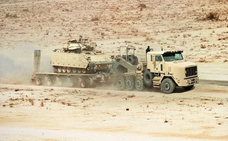 Un camión transporte de equipo pesado HET A1 traslada un vehículo blindado en un terreno desértico (Oshkosh Corporation )