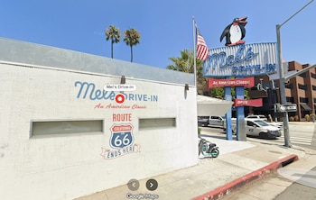 Edificio blanco con la inscripción Mel's Drive-In, un mural de la Ruta 66, un cartel con un pingüino y una bandera de Estados Unidos