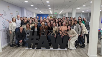 Una gran multitud de empleados de GroupM sonríen mientras posan detrás de las letras negras que forman #SOMOSAW, en una oficina moderna