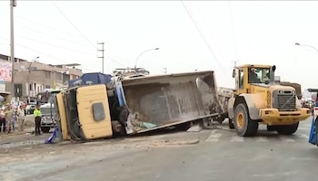 Un camión de carga amarillo volcado sobre su costado en una vía junto a maquinaria pesada y personal de emergencia al fondo