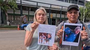 Una mujer y un hombre sostienen carteles de búsqueda en la calle. La mujer muestra un folleto de persona desaparecida; el hombre una foto de un joven