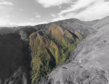 Vista aérea de montañas con una sección central verde rodeada de terreno en blanco y negro bajo un cielo nublado