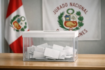 Urna electoral transparente con papeletas sobre una mesa de madera clara. De fondo, la bandera de Perú y el logo del Jurado Nacional de Elecciones.