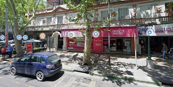 Fachada de un local de Crédito Mágico con cartel rosa, un automóvil azul estacionado en la calle y árboles en la acera