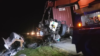 Camión grúa levanta restos de un vehículo con número catorce en la cabina; otro vehículo volcado en el pasto; luces de fondo y oscuridad