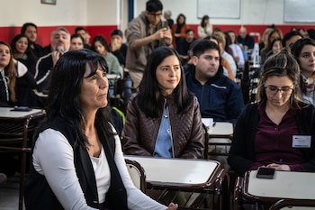 Decenas de personas sentadas en pupitres individuales dentro de un aula con computadoras portátiles y cuadernos