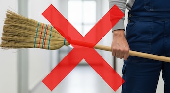 Primer plano de una persona vestida con un mono de trabajo azul, sosteniendo una escoba de paja, superpuesta por una gran X roja de prohibición.