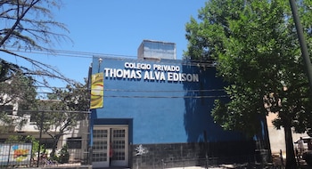Fachada azul de un edificio con el texto Colegio Privado Thomas Alva Edison en letras blancas, una puerta de entrada y árboles alrededor