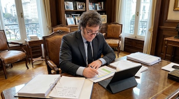 Un hombre con traje y anteojos trabaja en un escritorio con documentos sobre el presupuesto, carpetas y una tableta digital.