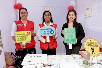 Tres mujeres sonrientes, dos con chalecos rojos de Inabif y una con blazer negro, sostienen carteles sobre familia y crianza en un evento