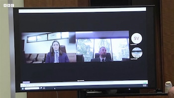 Un monitor muestra una pantalla de videollamada con tres participantes: un hombre de cabello largo y corbata, un hombre con gafas y dos avatares de perfil