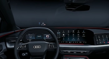 Volante multifunción con el logotipo de Audi frente a un panel de instrumentos digital, pantallas táctiles y proyección de datos sobre el parabrisas