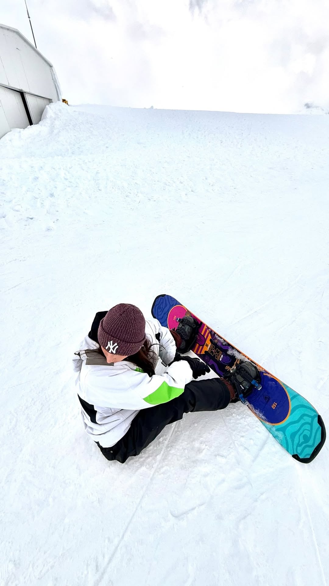 Carla Campos Salazar se sienta sobre la nieve para ajustar su tabla de snowboard durante un viaje fuera de Perú.