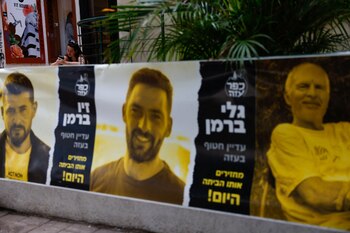 Una mujer utiliza su teléfono celular en Tel Aviv, cerca de los afiches con imágenes de los secuestrados por el grupo terrorista Hamas el 7 de octubre de 2023 (REUTERS/Carlos Garcia Rawlins)