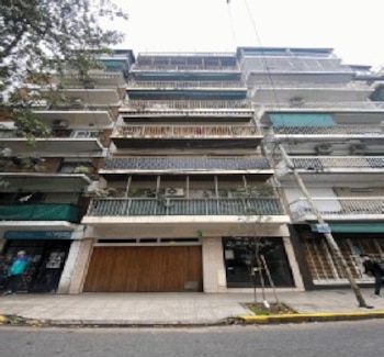 Fachada de un edificio de apartamentos de múltiples pisos con balcones, plantas, aires acondicionados y una puerta de garaje de madera en la planta baja