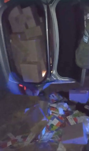 Maletero abierto de un Hyundai Elantra con múltiples cajas de cartón apiladas. En el suelo junto al coche se ven más cajas y objetos de colores, iluminados por una luz azul