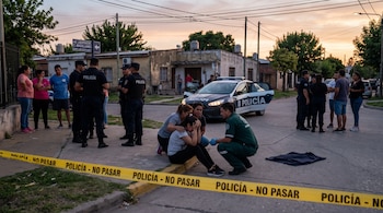 Policías y un médico atienden a una joven sentada en la acera detrás de una cinta amarilla de seguridad en un cruce de calles.