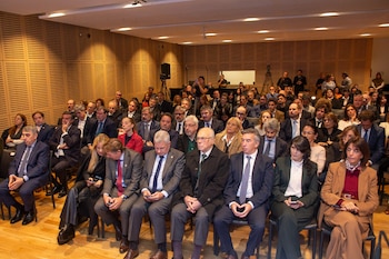 Uma visão geral de uma sala de conferências com dezenas de participantes sentados em filas, a maioria homens e mulheres em trajes formais