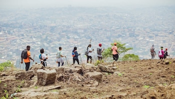 Un grupo de personas con mochilas y bastones de senderismo camina por la cumbre de una colina sobre un paisaje urbano
