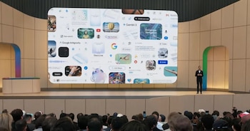 Sundar Pichai, CEO de Google, de pie en un escenario frente a una pantalla gigante que exhibe múltiples interfaces de software de Google, con una audiencia visible