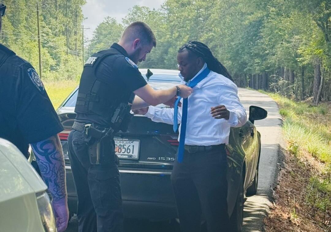 Un policía ayuda un conductor a ajustarse su corbata. (St. Tammany PArish Sheriffs