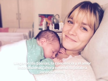 Rocío Igarzábal, de pelo rubio con flequillo, sonríe suavemente mientras un bebé duerme plácidamente acurrucado en su pecho, cubierto con una manta