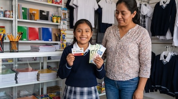 Una niña mexicana con uniforme escolar y su madre en una tienda. La niña sonríe, sosteniendo una tarjeta del Banco del Bienestar y billetes de 200 y 500 pesos.