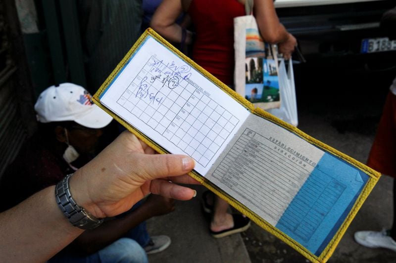 Una mujer muestra su libro de raciones, conocido localmente como la