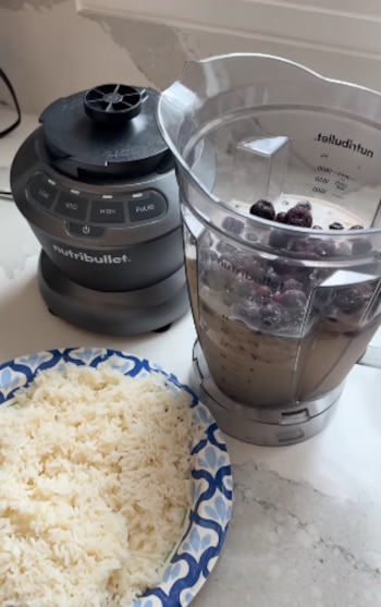 Una jarra de licuadora con frutos rojos sobre una base gris, junto a un plato con arroz blanco cocido
